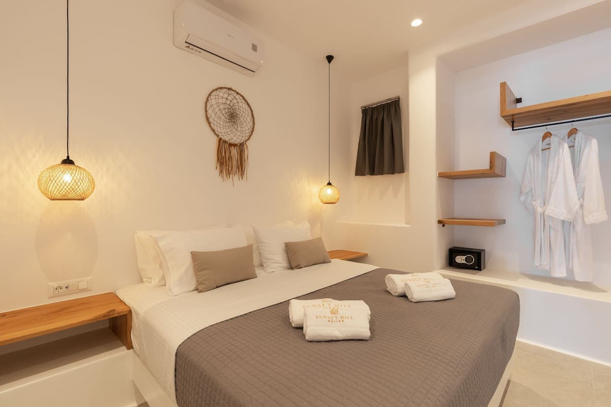 A modern bedroom with a bed, bedside lamps, a dreamcatcher, a wall-mounted air conditioner, a radio, and a robe rack with towels.