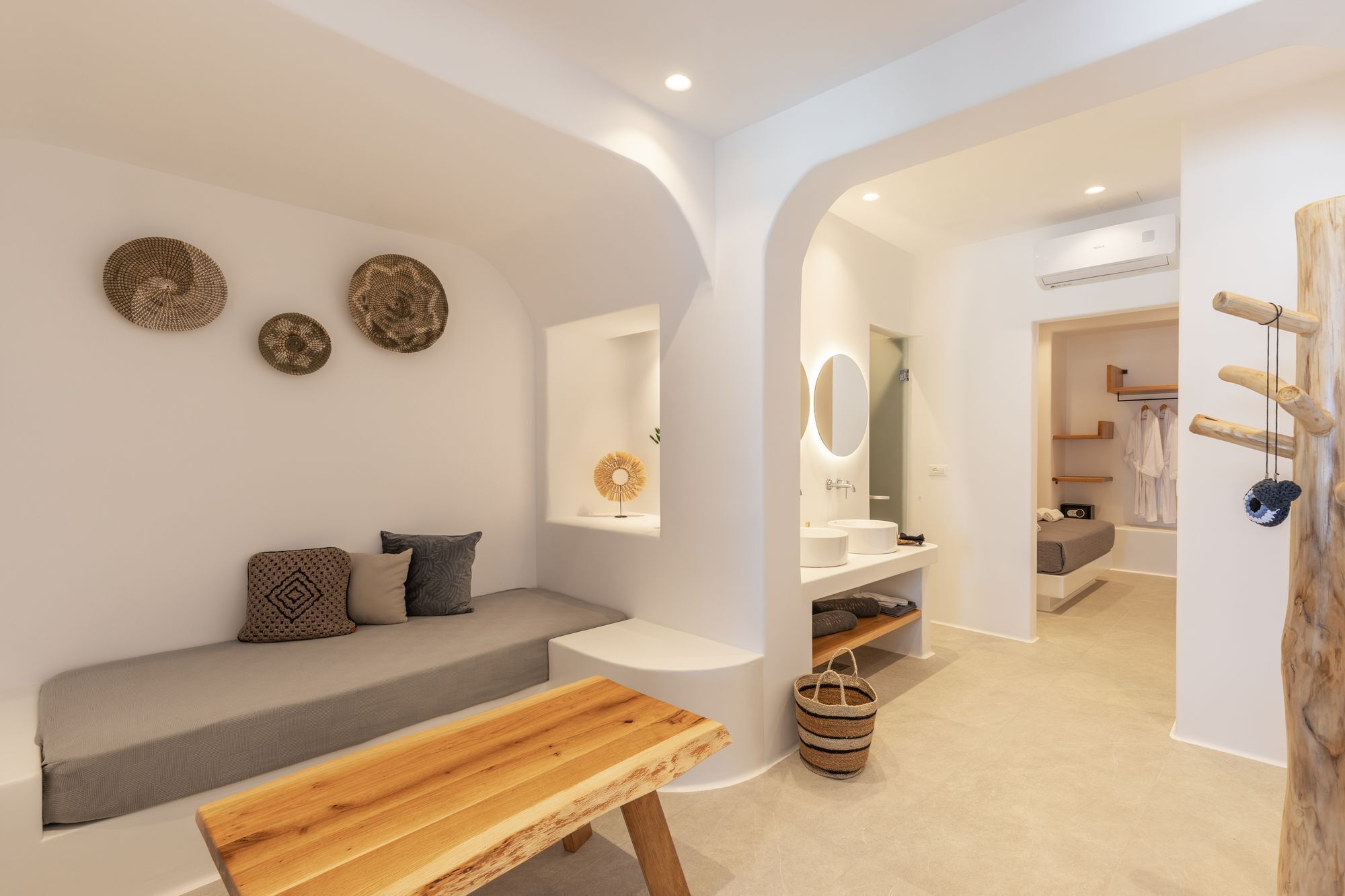 A modern, minimalist bathroom with a wooden bench, a small table, and a wall-mounted vanity.