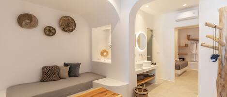 A modern, minimalist bathroom with a wooden bench, a small table, and a wall-mounted vanity.