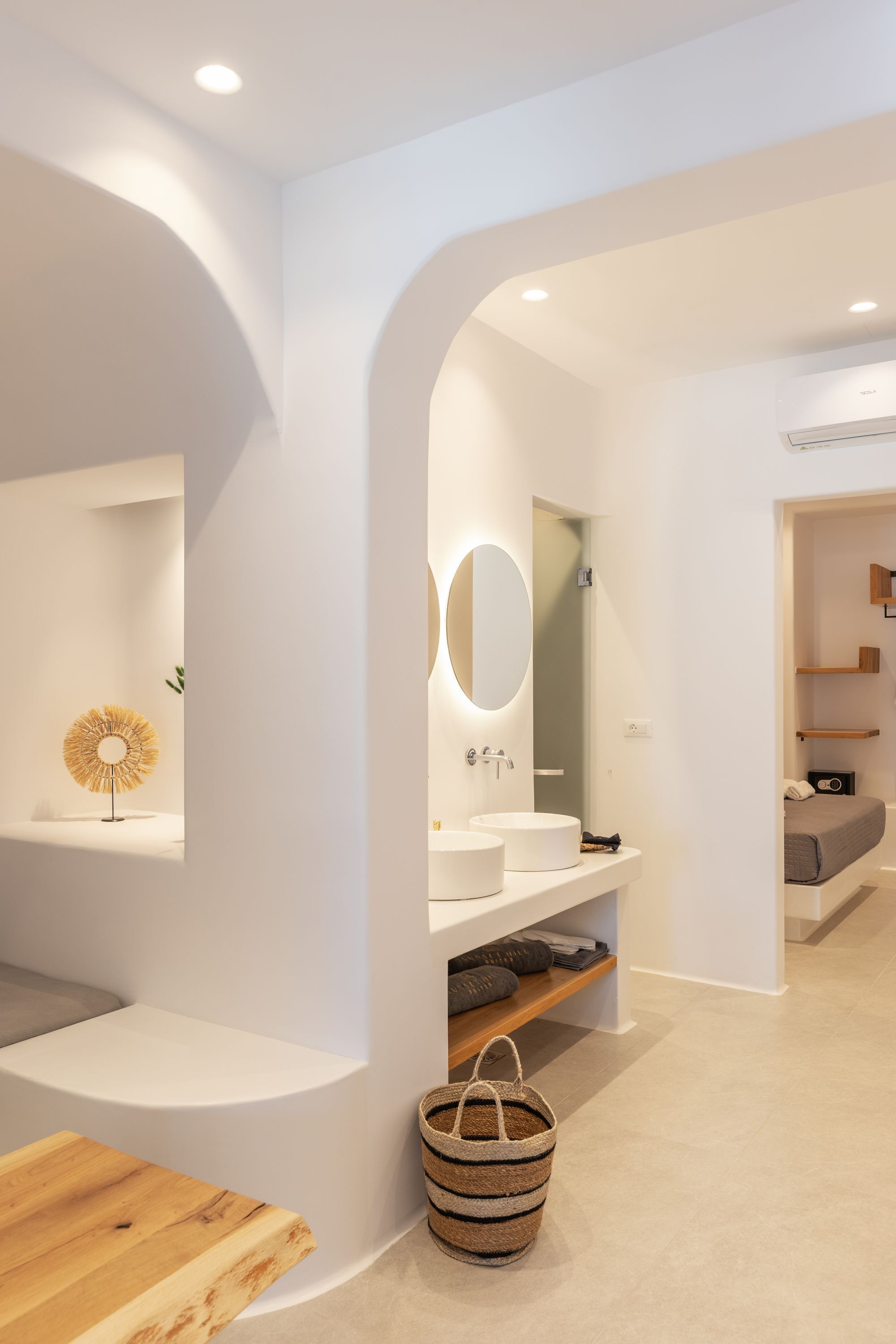 Een moderne badkamer met een ronde spiegel, twee wasbakken en een houten bankje.