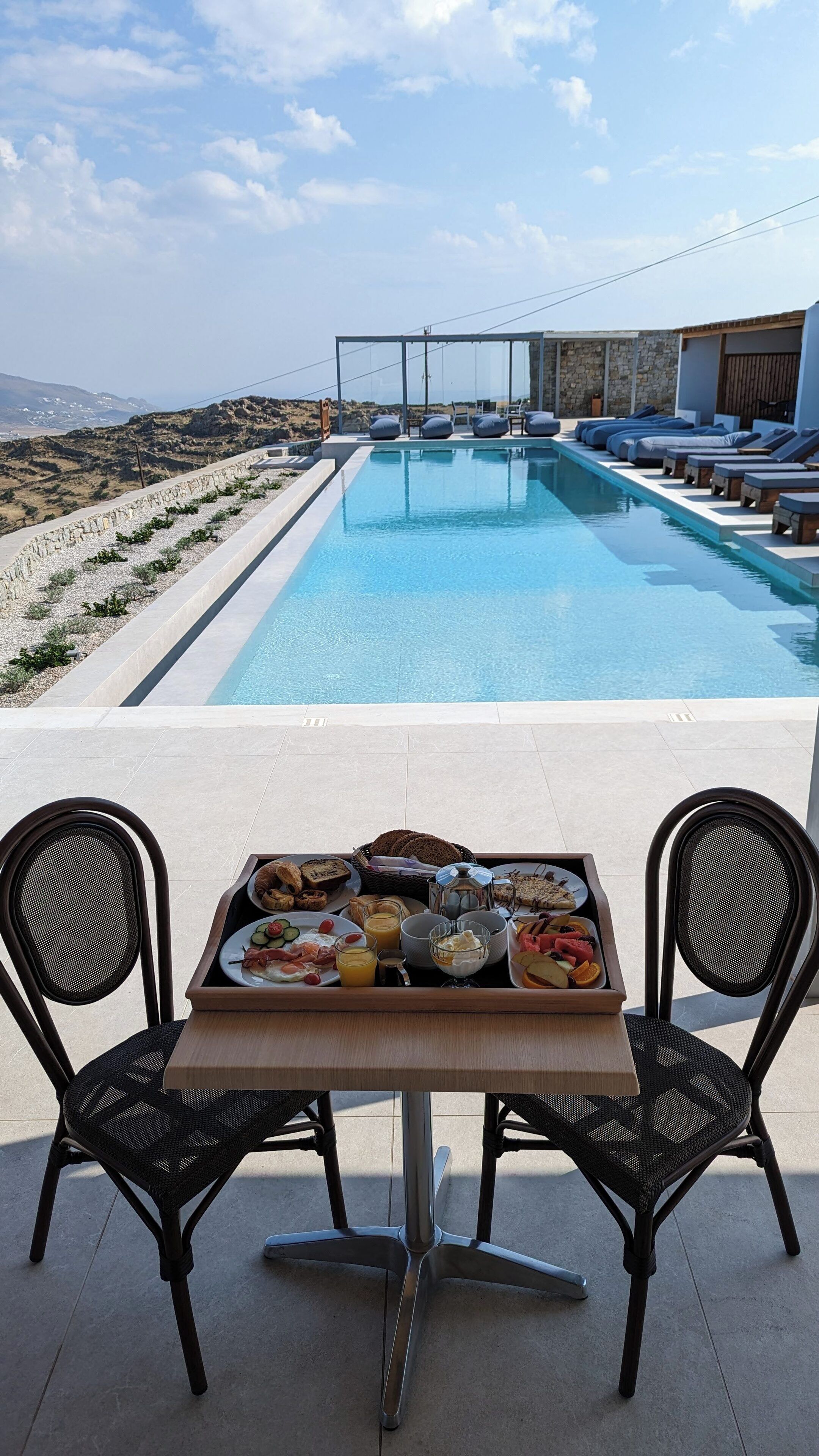 A poolside dining area with a table set for breakfast, overlooking a swimming pool and a scenic landscape.