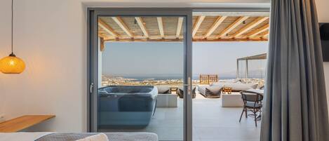 A bedroom with a large sliding glass door leading to an outdoor seating area with a view of the sea.