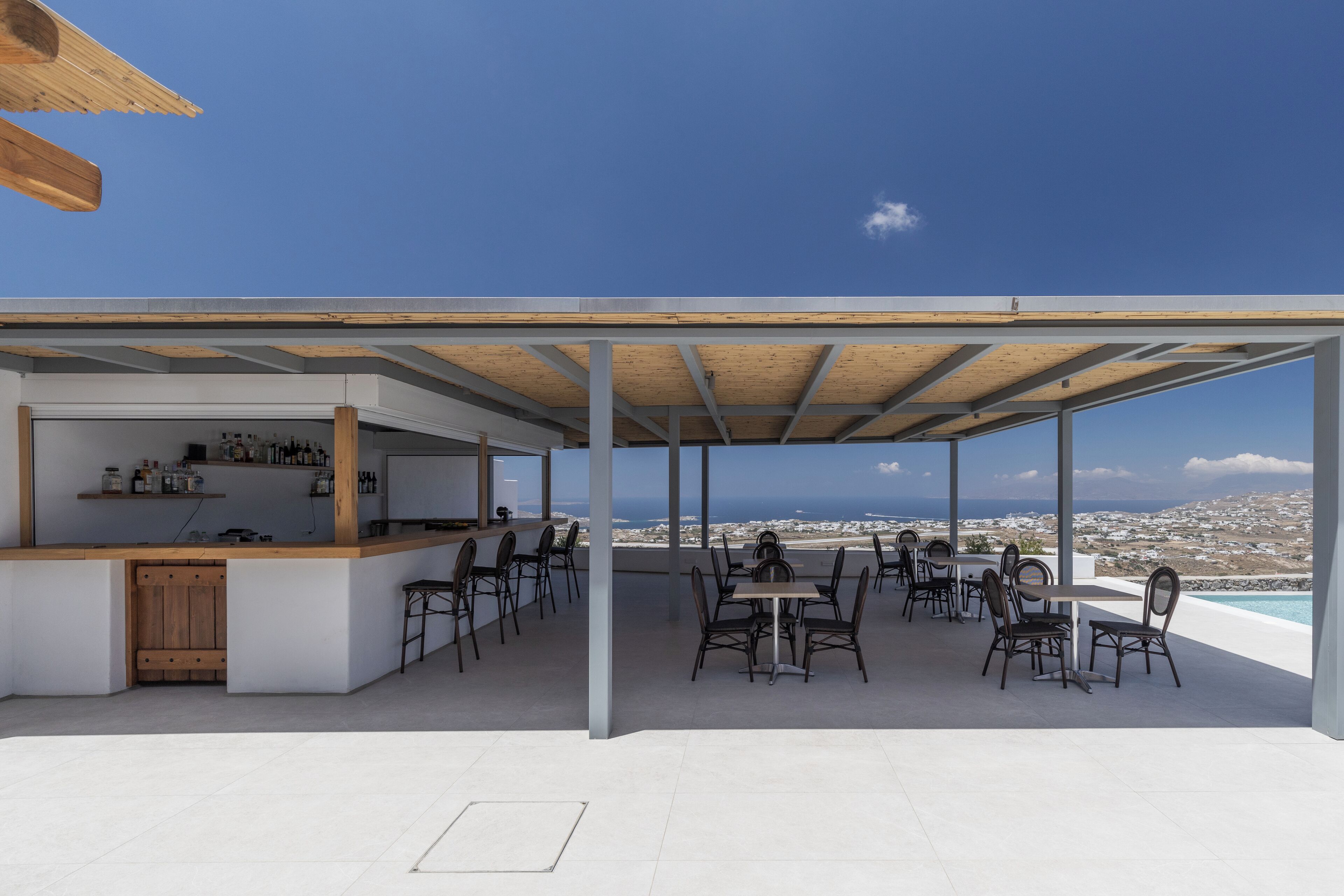 An outdoor dining area with a view of the sea, a bar, and a pool.