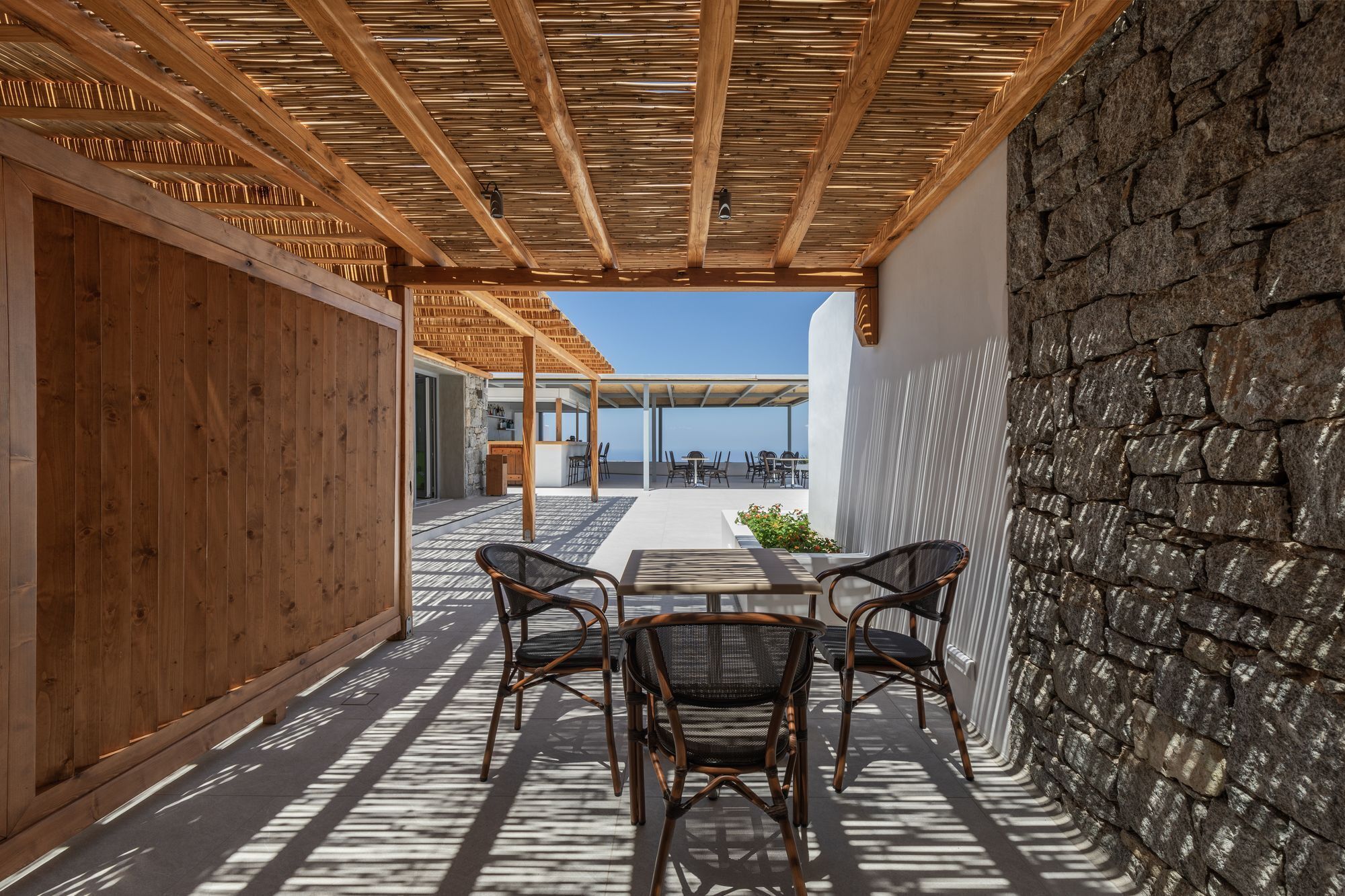 A covered outdoor seating area with wicker chairs and a stone wall.