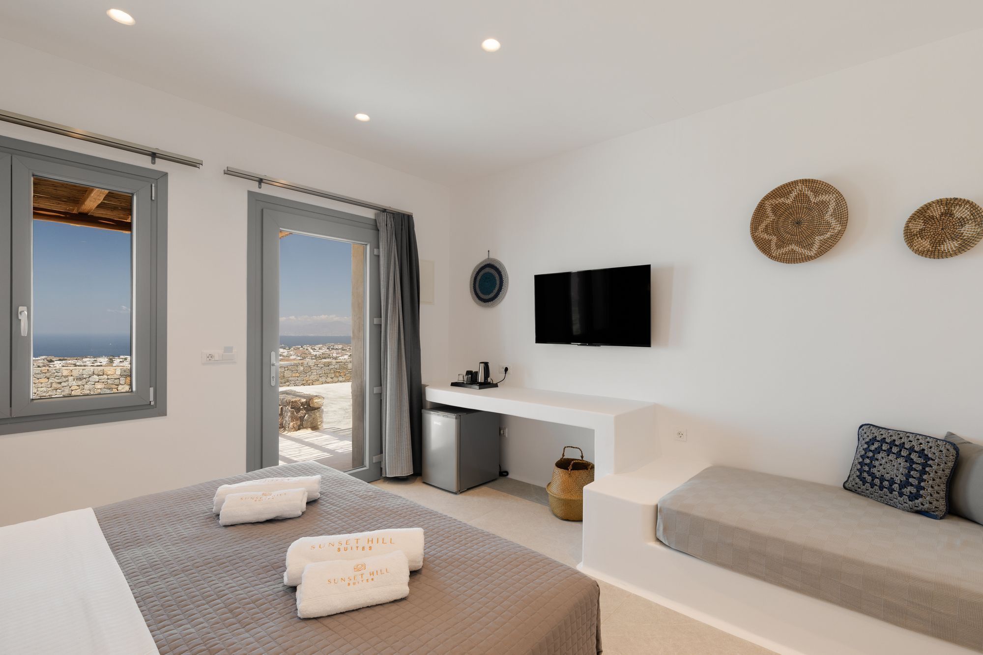 A modern hotel room with a bed, a sofa, a desk, and a TV.
