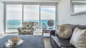 Un'ampia zona giorno con balcone vista mare, un divano in pelle, una poltrona a fantasia e un tavolino con oggetti decorativi.