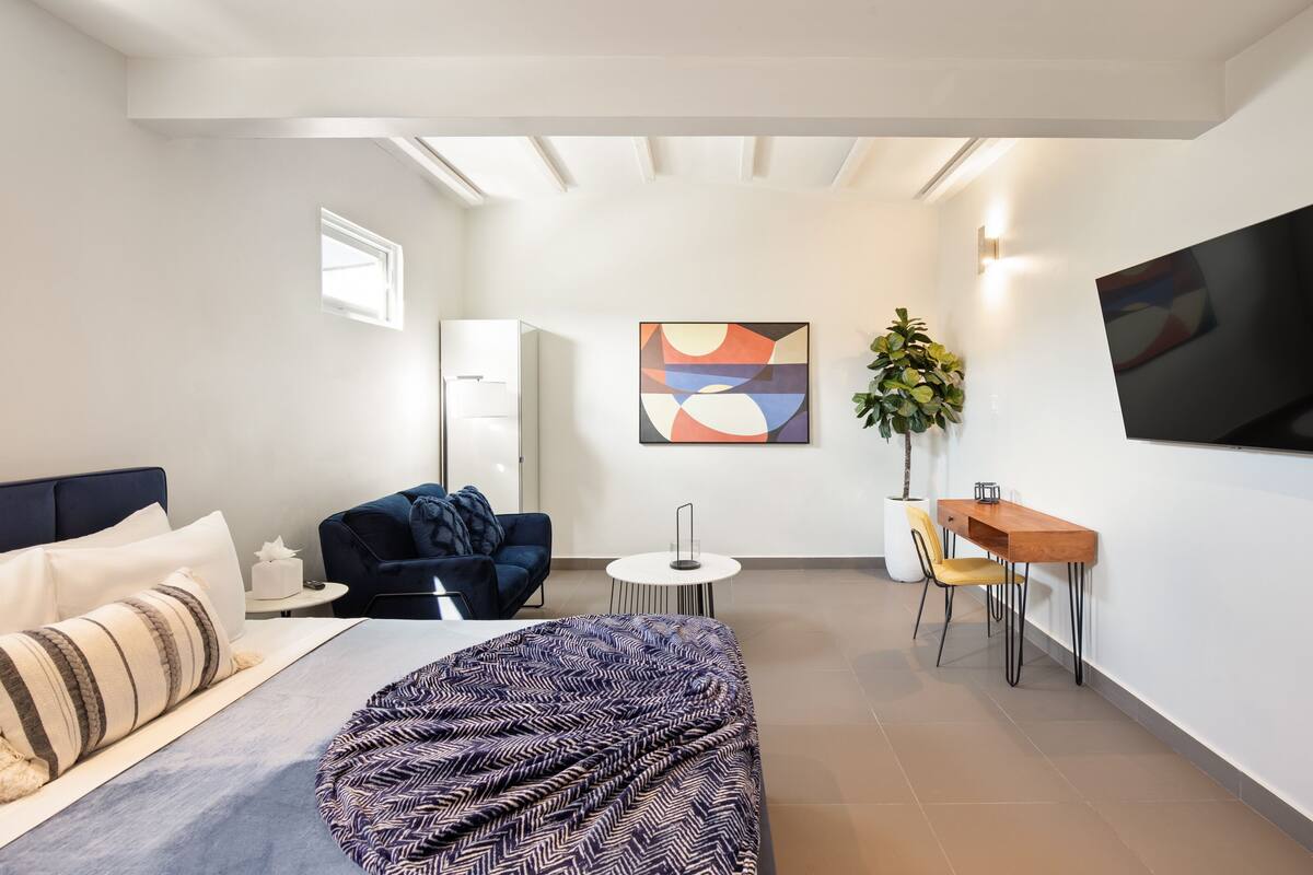 A modern bedroom with a bed, a sofa, a desk, and a TV.