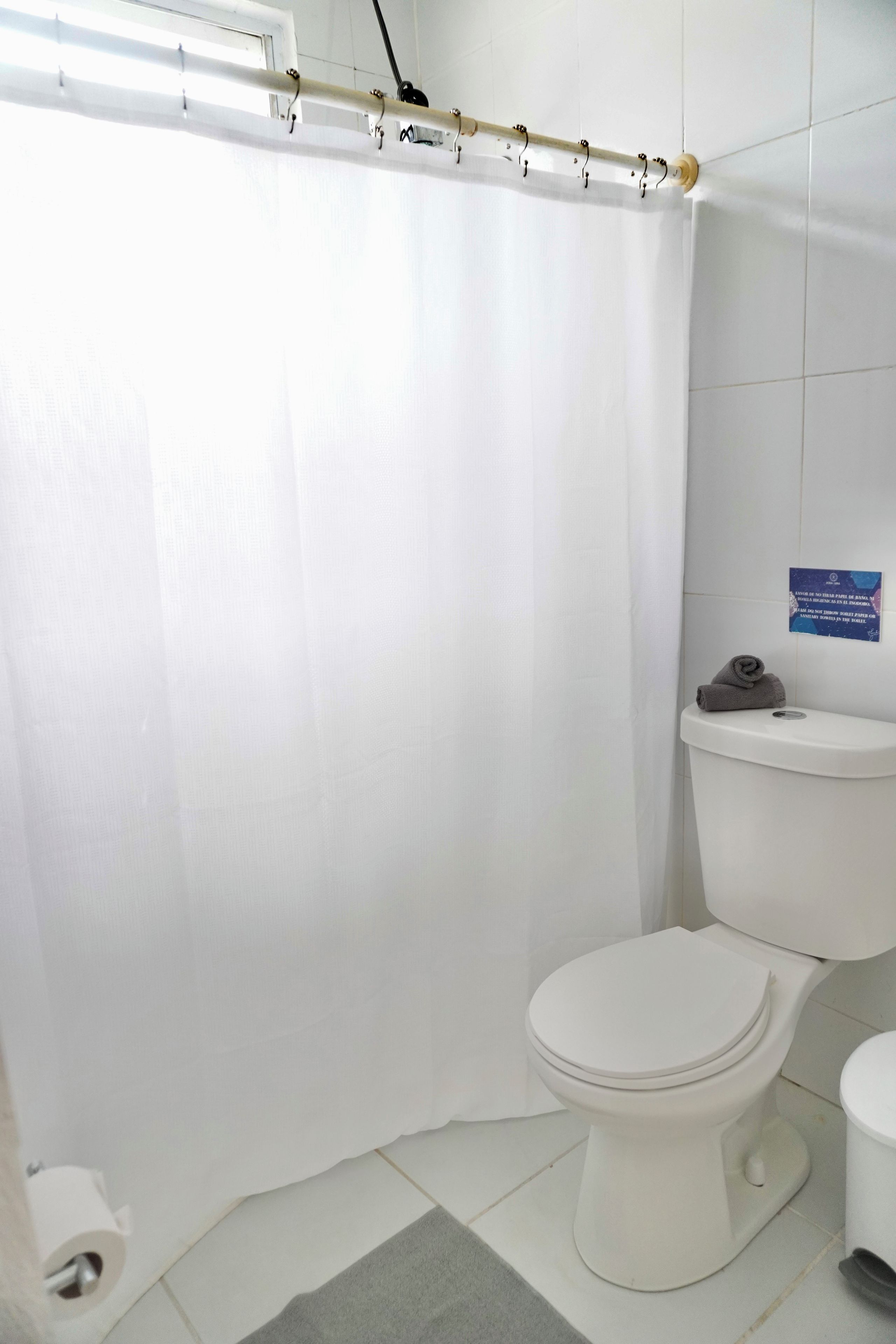 A bathroom with a white toilet, a shower curtain, and a sign on the wall.