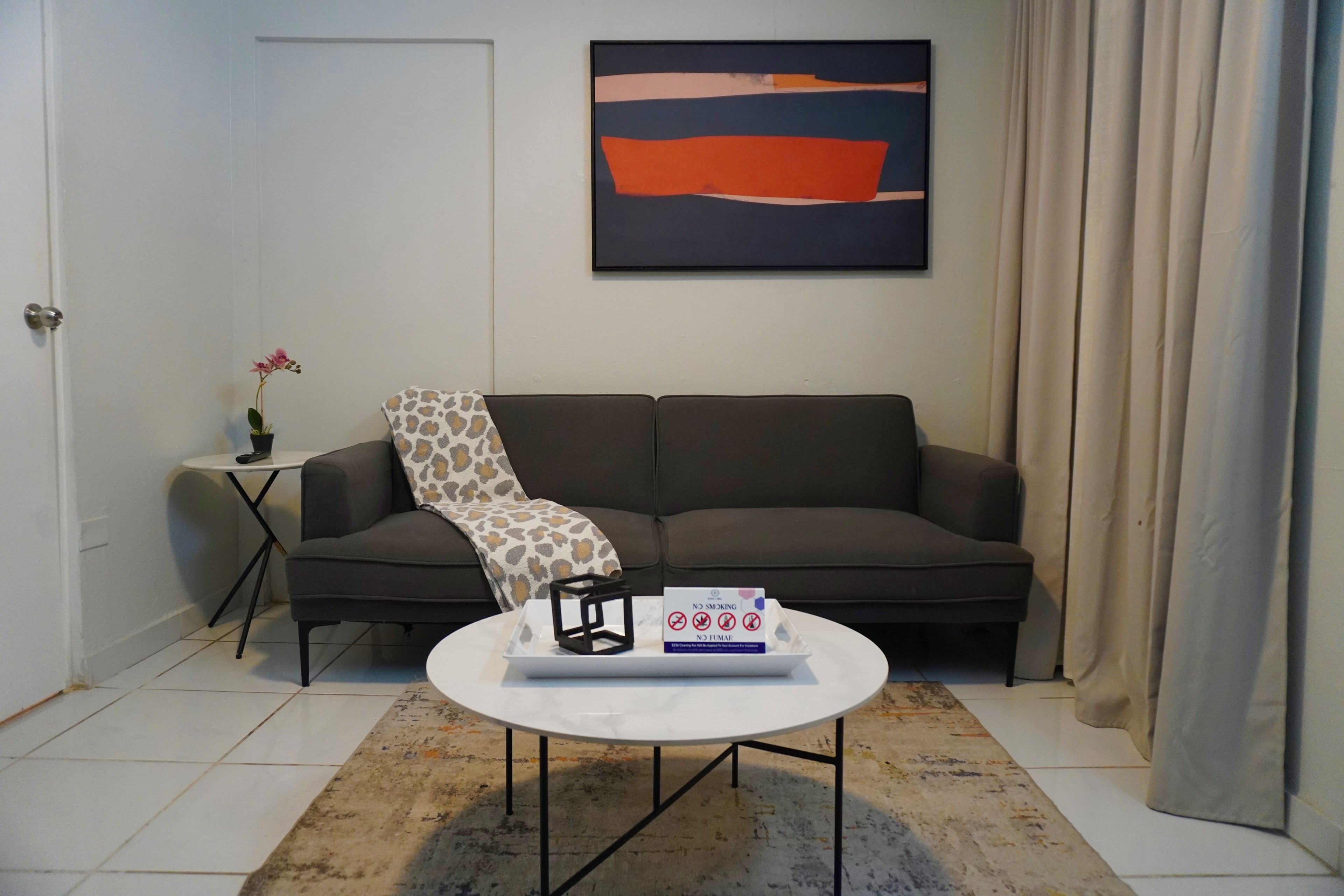Una sala de estar con un sofá, una mesa de centro, una mesita auxiliar con una planta y un cuadro en la pared.