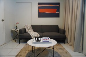Uma sala de estar com um sofá, uma mesa de centro, uma pequena mesinha lateral com uma planta e um quadro na parede.