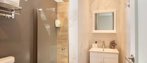 A modern bathroom with a glass-enclosed shower, a vanity with a marble countertop, and a large mirror above the sink.