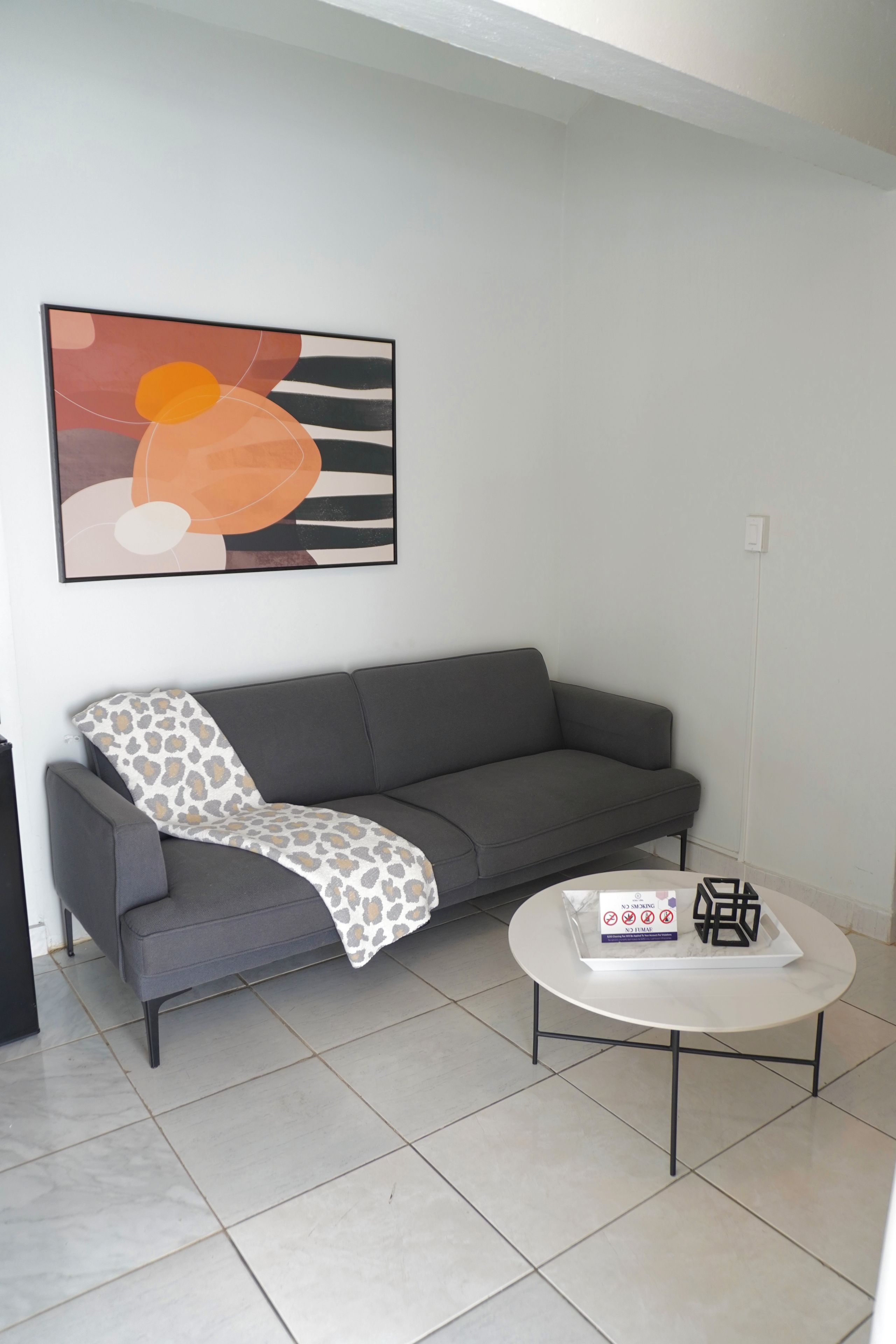 Un salon moderne avec un canapé gris, une table basse blanche et un tableau abstrait accroché au mur.