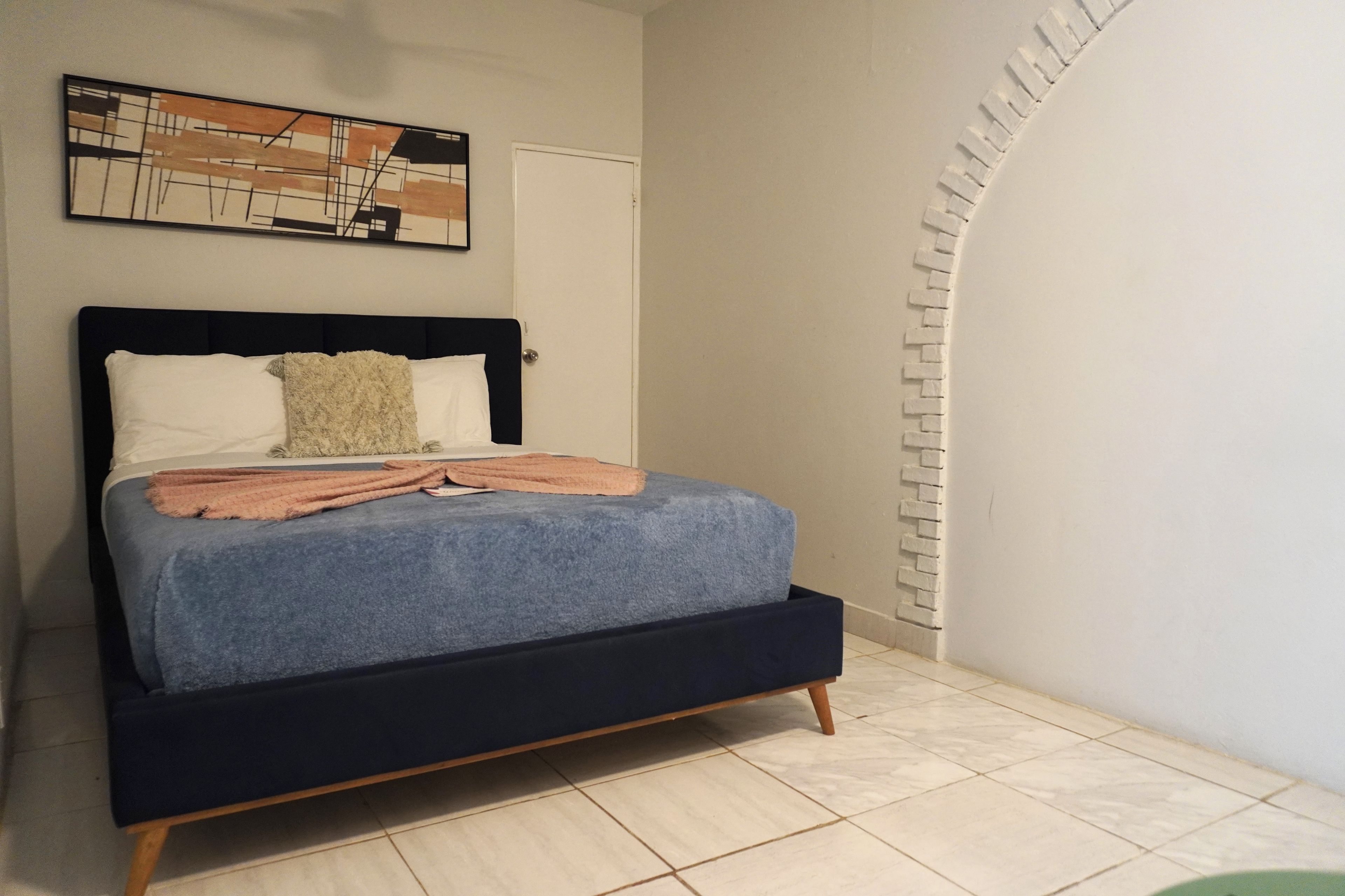 A bed with a dark headboard, white and beige pillows, and a blue blanket.