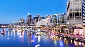 A waterfront cityscape with modern high-rise buildings, a marina with boats, and a pedestrian walkway along the river. - Neogaia Bed & Breakfast (West Pennant Hills)