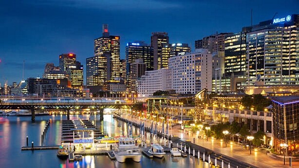 A waterfront cityscape with modern buildings, a marina with boats, and a bridge. - Neogaia Bed & Breakfast (West Pennant Hills)