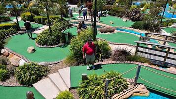 A miniature golf course with a pool, surrounded by tropical plants and a wooden bridge.