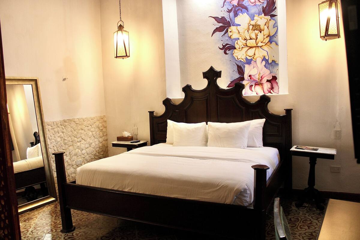 A neatly made bed with white linens, a wooden headboard, and a nightstand with a lamp.