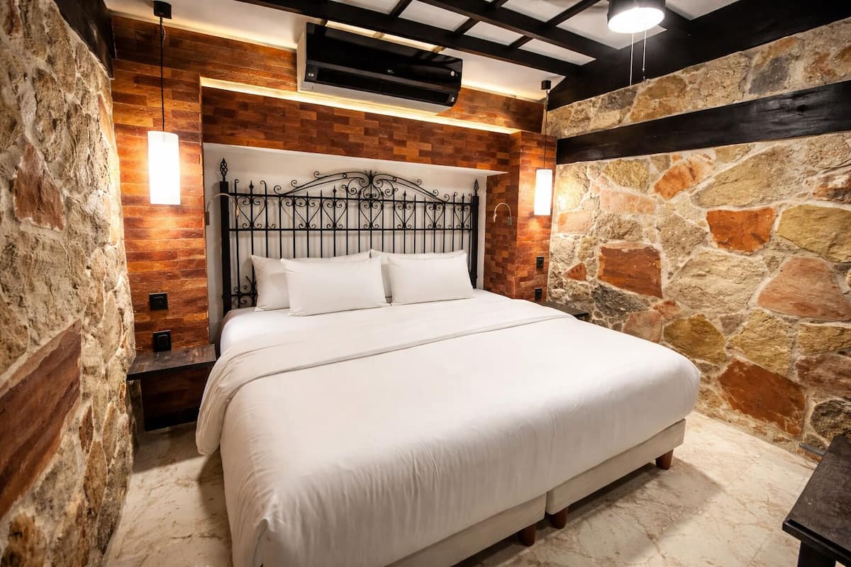 A bed with a headboard, white bedding, and a stone wall.