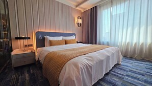 Une chambre d’hôtel avec un grand lit, une table de chevet, une lampe et une fenêtre avec des rideaux.