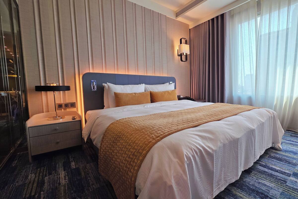 Een hotelkamer met een groot bed, een nachtkastje, een lamp en een raam met gordijnen.