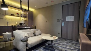 Une chambre d’hôtel moderne équipée d’un canapé, d’une petite table ronde, d’une machine à café et d’un téléviseur fixé au mur.