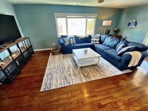 A living room with a sectional sofa, a coffee table, a TV stand, and a large window.