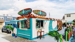 Un petit camion-restaurant aux couleurs vives, baptisé « Soulberry », avec une façade bleue et blanche, est garé sur un parking où se trouvent quelques personnes et une voiture à proximité.
