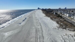 Une plage avec un ciel dégagé, un rivage sablonneux et des bâtiments en arrière-plan.