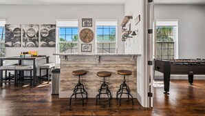 Une cuisine moderne avec un coin bar, des tabourets en bois, une table de baby-foot et de grandes fenêtres.