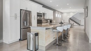 Une cuisine moderne avec des meubles blancs, des appareils en acier inoxydable, un comptoir en granit et un coin bar avec des tabourets blancs.
