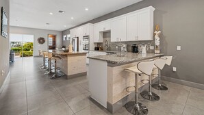 Une cuisine moderne avec des meubles blancs, des plans de travail en granit et des tabourets de bar.