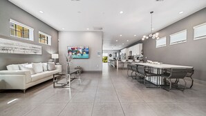 Un grand espace de vie comprenant un canapé blanc, une table à manger avec des chaises, et une cuisine en arrière-plan.