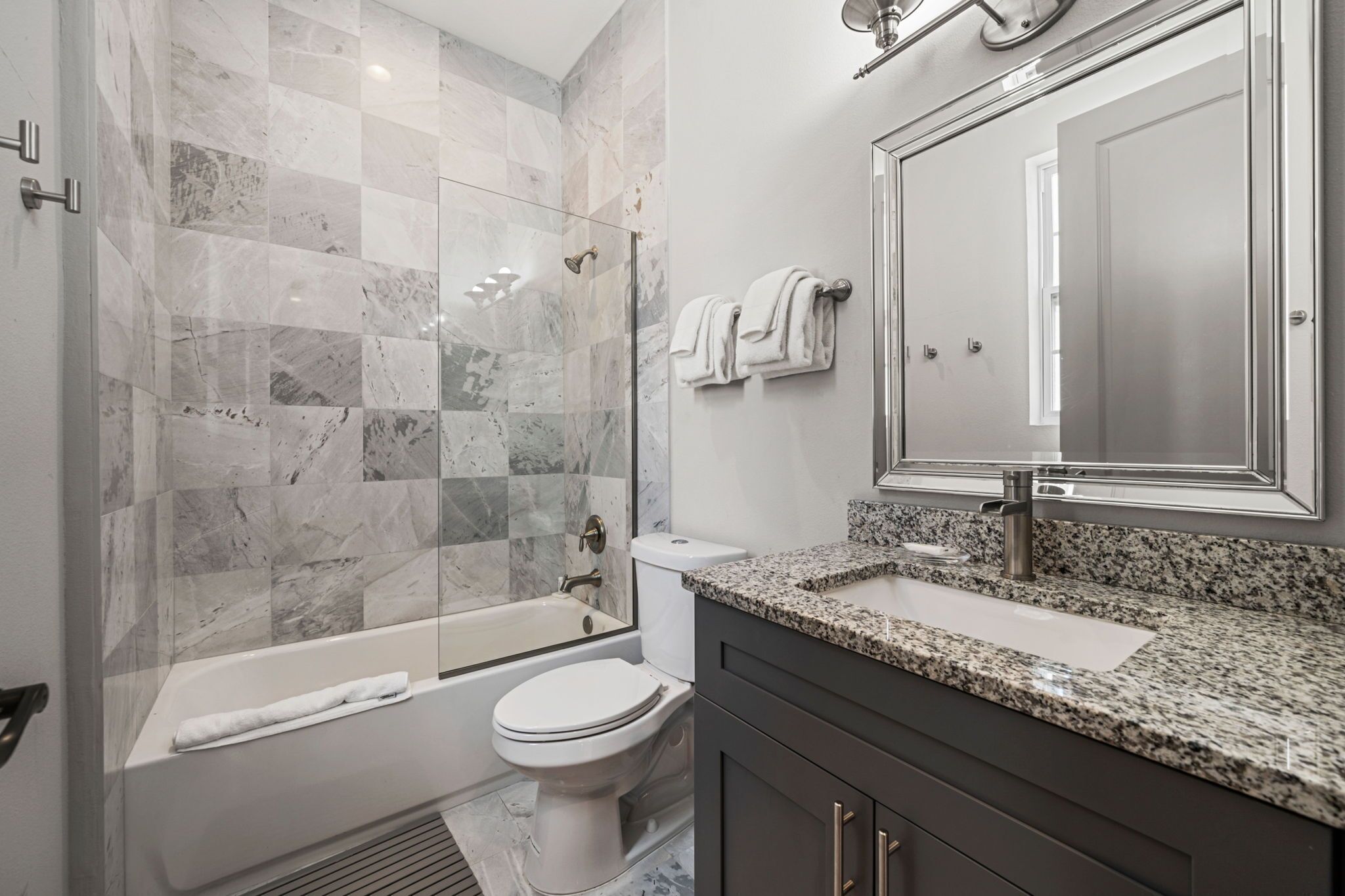 A modern bathroom with a glass-enclosed shower, a bathtub, a toilet, and a sink with a granite countertop.