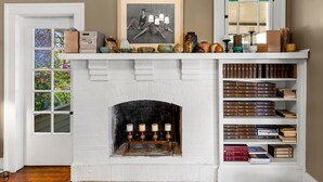 Ein weißer Kamin aus Backsteinen mit Kaminabdeckung, auf der Bücher, Dekorationen und ein schwarz-weißes Foto gerahmt sind.