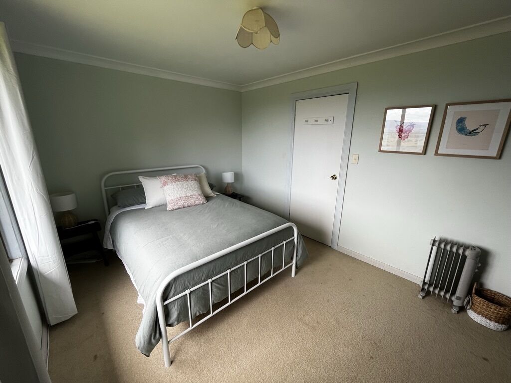 A bedroom with a single bed, a radiator, a door, and framed pictures on the wall.