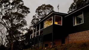 Une maison moderne à deux étages, dotée d’un balcon et entourée d’arbres.
