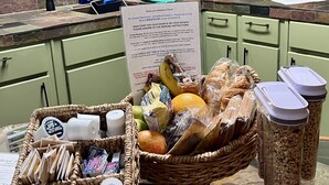 Una encimera de cocina con una cesta de mimbre que contiene alimentos, un recipiente de plástico con tapa y un letrero con indicaciones de estacionamiento.