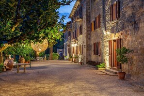 Un bâtiment en pierre avec une cour recouverte de gravier, des plantes en pot et des sièges à l’extérieur.