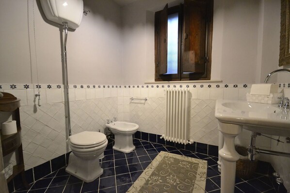 Une salle de bain avec deux toilettes, un lavabo, un radiateur et une fenêtre située au-dessus du lavabo.