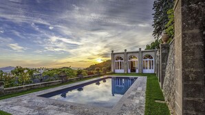 Uma piscina com borda de pedra, um edifício com janelas em arco e vista para a paisagem.