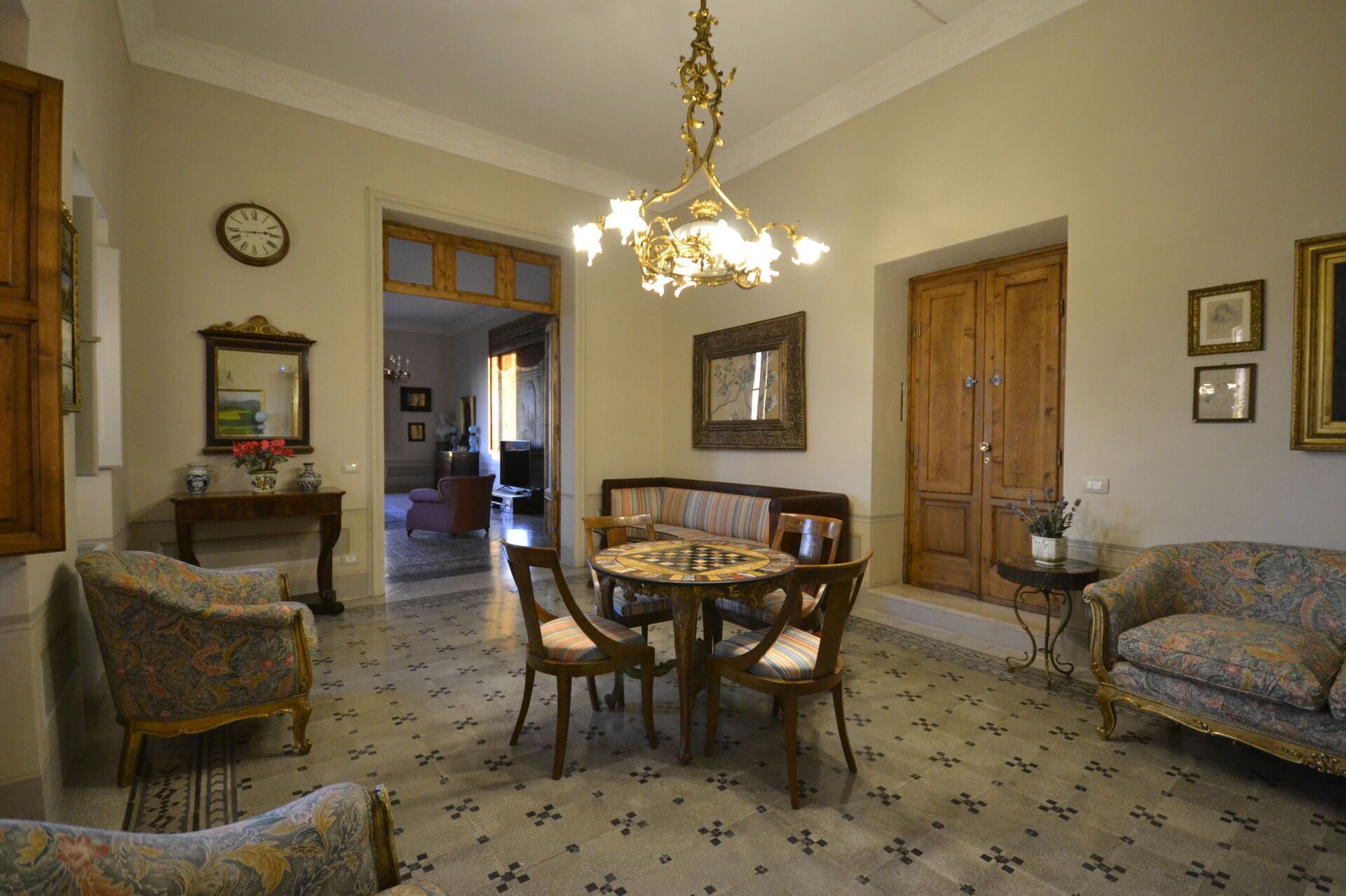 Un salón amplio con una mesa redonda, varias sillas, una lámpara de araña y una puerta grande de madera.