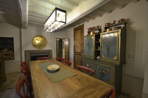 Un comedor con una mesa de madera, sillas rojas, una chimenea y un armario con ollas de cobre.