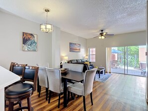A spacious living area with a dining table, chairs, a sofa, and a ceiling fan.