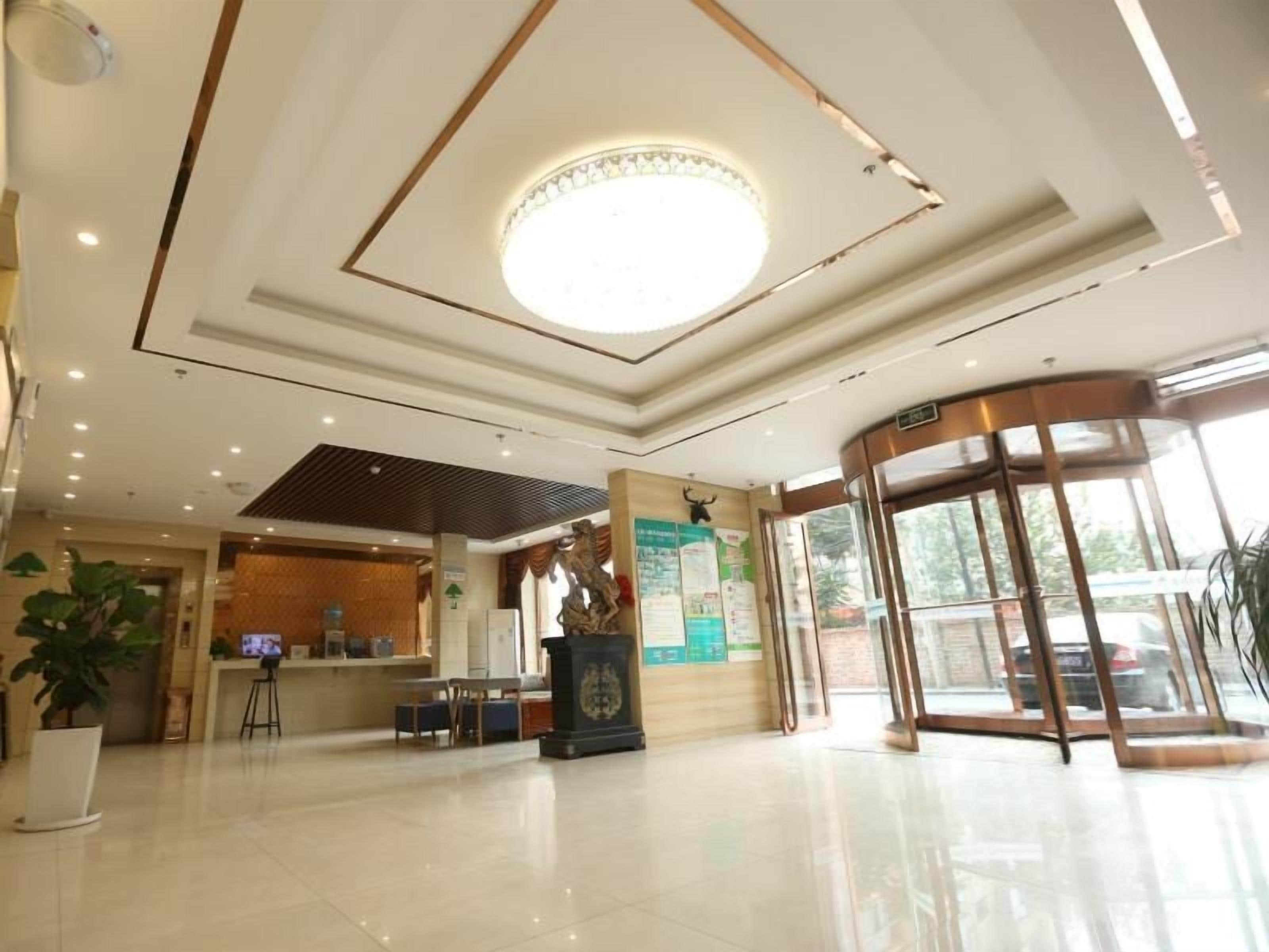Een hotel lobby met een receptiebalie, een grote ronde lamp, een glazen lift en een potplant.