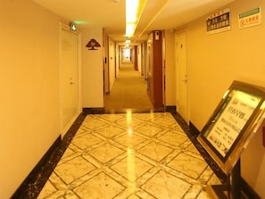 Corredor de hotel com piso ladrilhado, portas em ambos os lados e placas nas paredes.