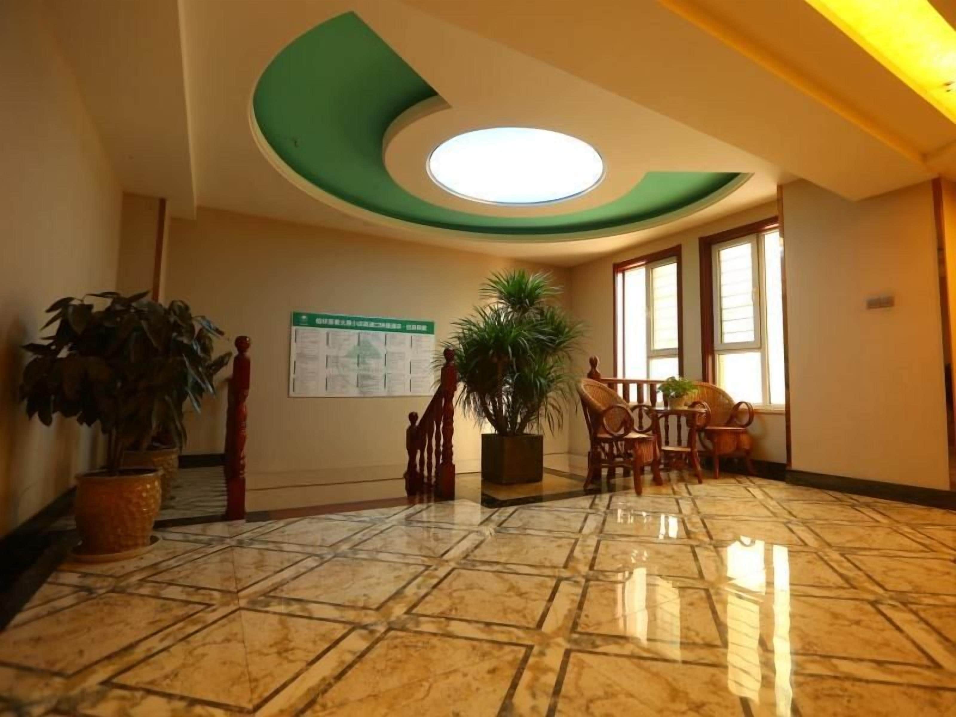 Un hall con suelo de mármol, techo verde, una escalera y una zona de estar con sillas y una mesa.