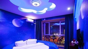 Una habitación con una cama en una estructura azul circular, una ventana con vistas y una pequeña mesa con sillas.