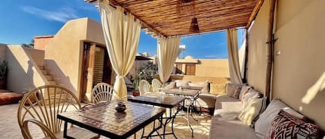 Une terrasse extérieure avec une table, des chaises et un canapé, le tout abrité par un toit en bambou.