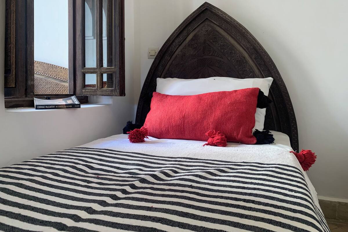 Un lit avec une couvre-lit à rayures, un oreiller rouge et une tête de lit en bois foncé.