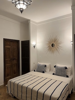 A bedroom with a bed, two wall sconces, a decorative mirror, and wooden doors. - Riad Laksiba (Marrakech)